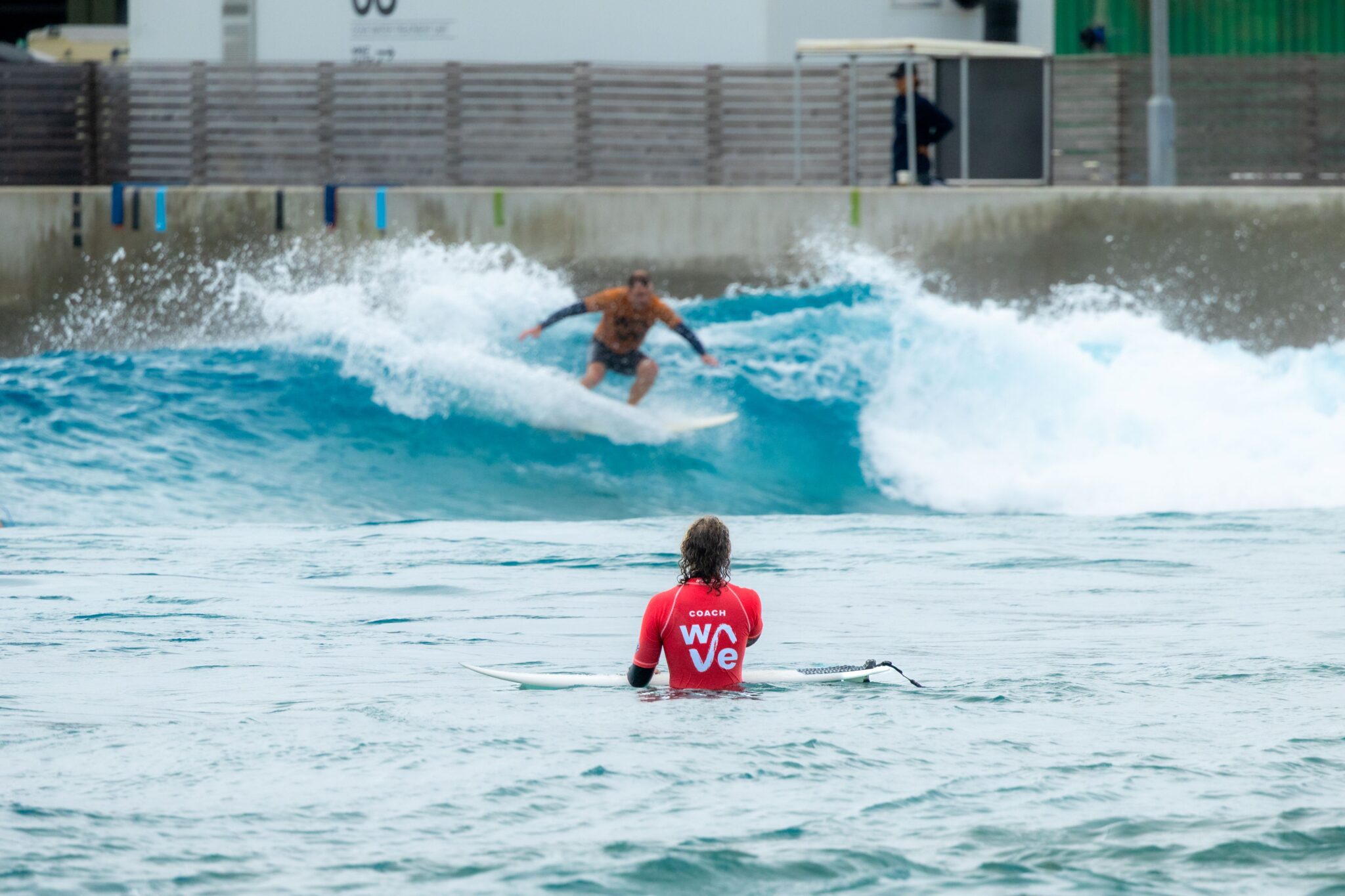 A surfer rides an Advanced wave, while a coach gives feedback in the water.