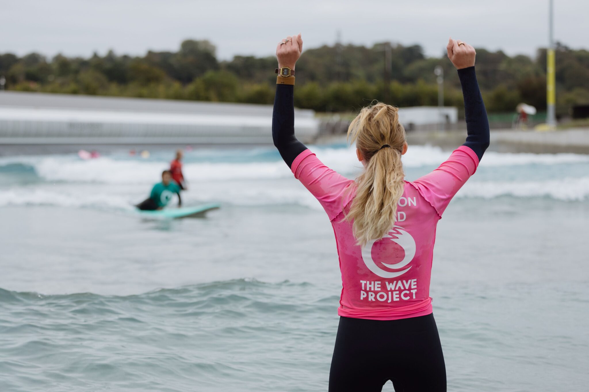 A coach from The Wave Project cheers on a surfer in the waves.