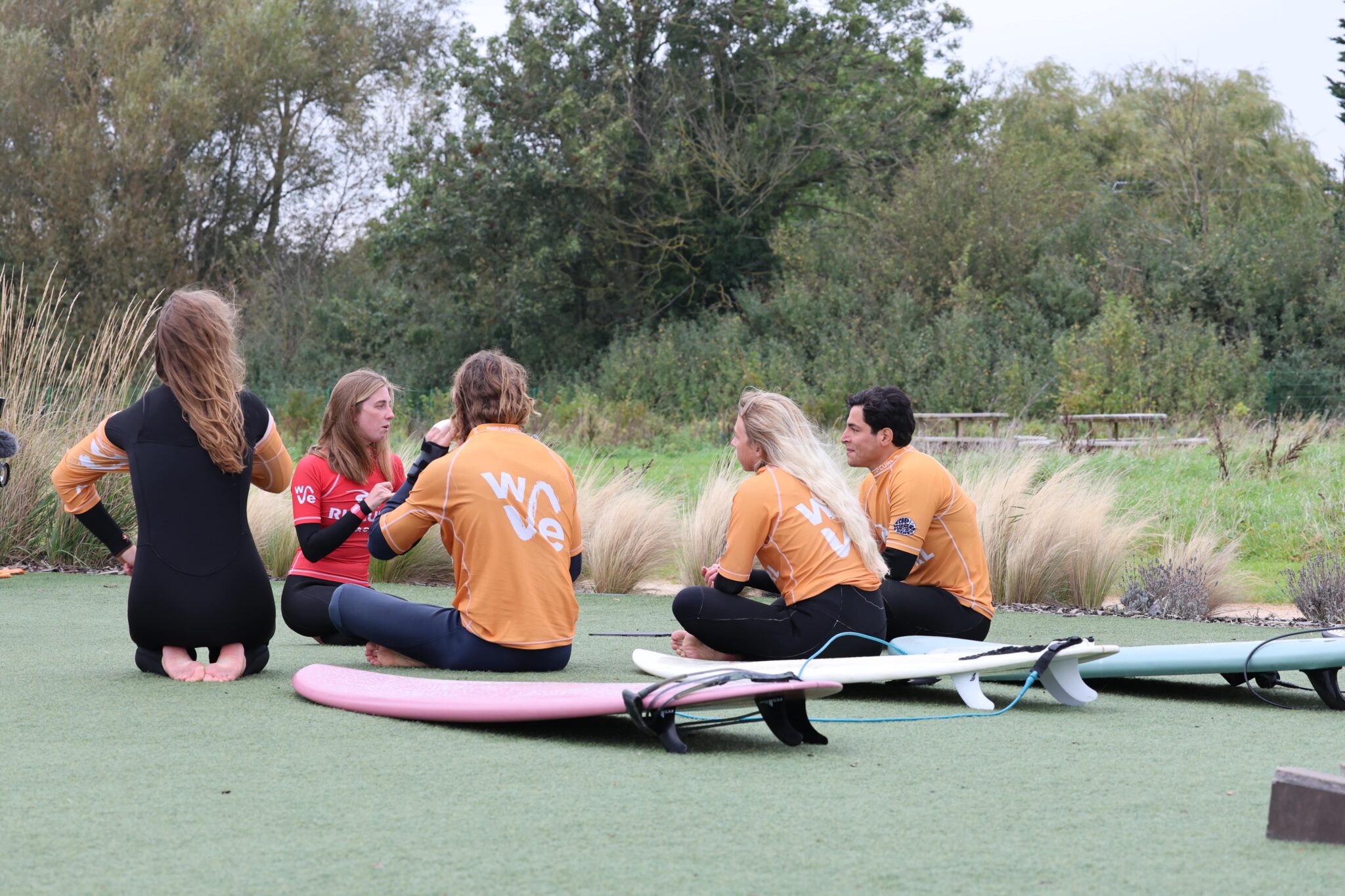 A group of surfers sit in a circle while listening to instructions from a coach at The Wave Bristol.
