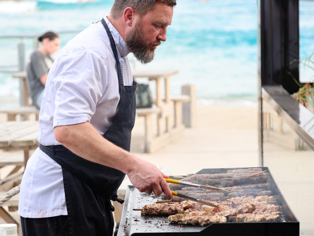 A chef barbeques food on a grill outside at The Wave Bristol.